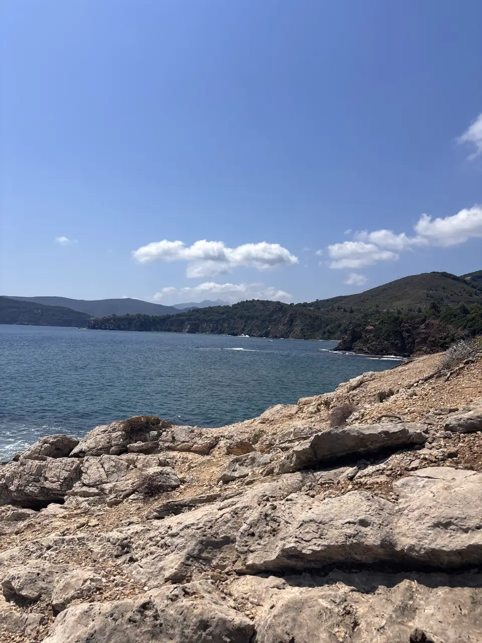 Von flachen Felsplatten am Wasser der weite Blick über die Bucht auf bewaldete Hügel am gegenüberliegenden Ufer.