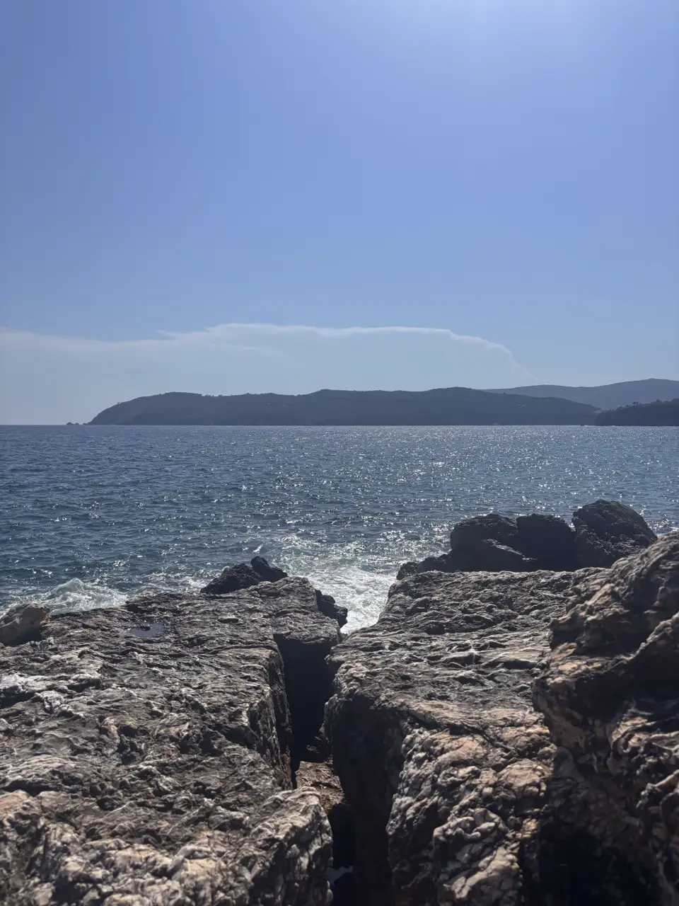 Von der Felskante der Blick über das Wasser auf eine Landzunge, die weit ins Meer hinausläuft.