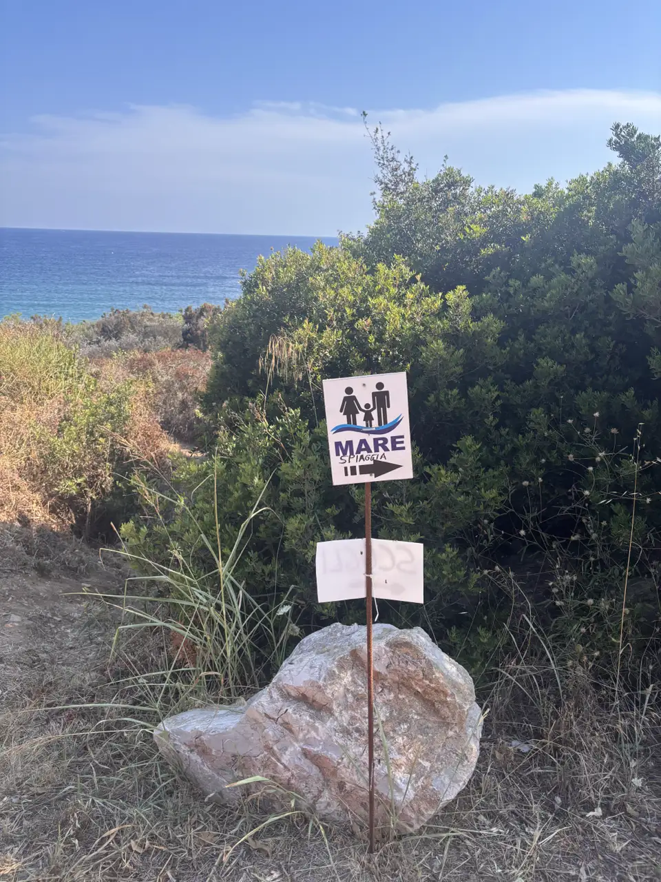 Ein Wegweiser mit der Aufschrift MARE und einem Piktogramm zweier Personen, daneben ein heller Stein.